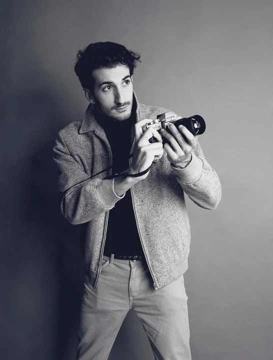 Marco Miraglia holding a Minolta 35mm film camera — black and white portrait from his Paris years