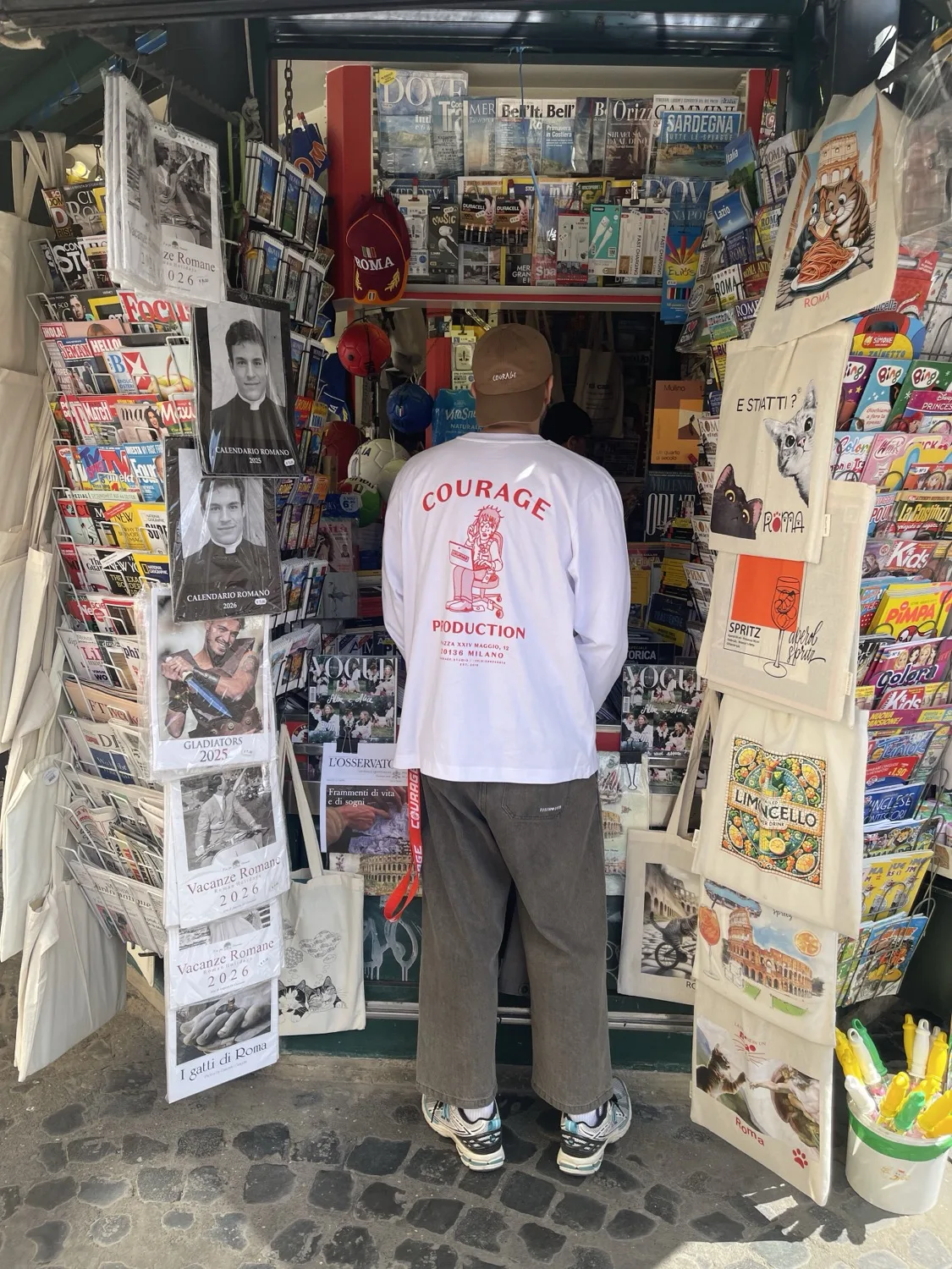 Courage Milano SS25 — tee and cap worn at a Roman newsstand